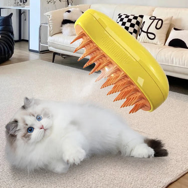 A fluffy white cat on a rug looks up at a floating KittyNook Cat Co. Electric Cat Grooming Brush with orange bristles.
